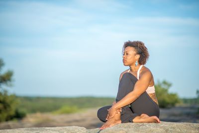 Full length of woman looking away while sitting on land against sky