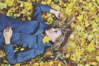Directly above shot of mid adult woman lying on maple leaves during autumn