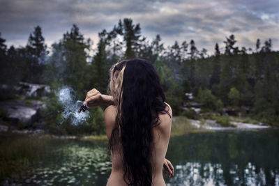 Rear view of woman standing by lake against trees