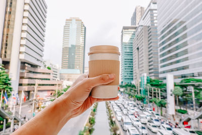 Midsection of person holding drink against buildings in city