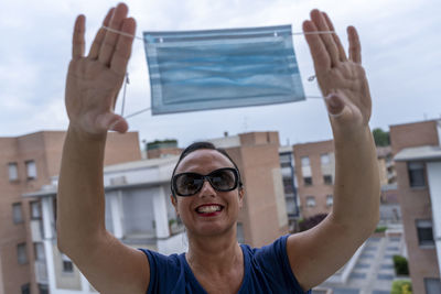 Pretty woman on the balcony of her home shows how to wear the anti covid-19 protection mask