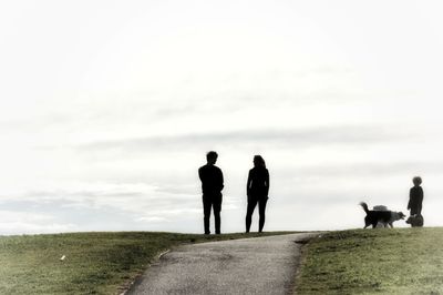 Silhouette people walking with dog on landscape against sky