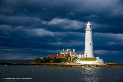 Lighthouse amidst sea and buildings against sky