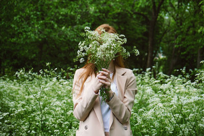 Young woman holding flower while standing by tree