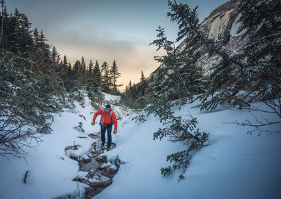 A male climber hops across rocks in a stream with sunrise behind him