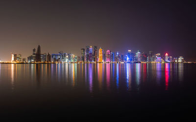 Illuminated buildings of doha city against sky at night