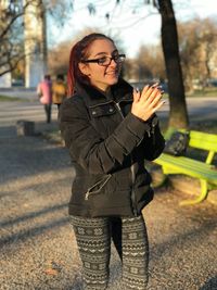 Smiling young woman clapping while standing in park