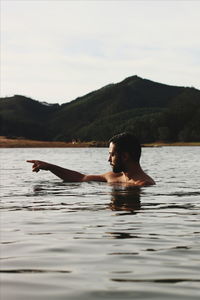 Shirtless man gesturing while swimming in lake