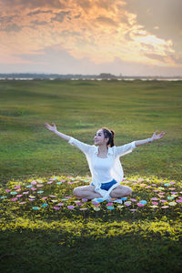 Woman with arms raised on field against sky during sunset