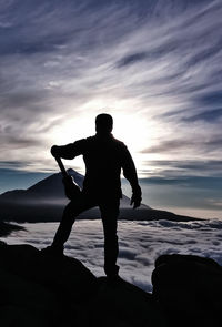 Silhouette man standing on rock against cloudy sky during sunset