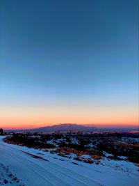 Snow covered landscape against clear sky during sunset