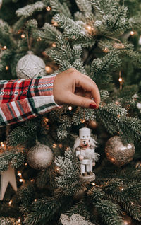 Close-up photo of female hand decorating christmas tree with nutcracker soldier ornament