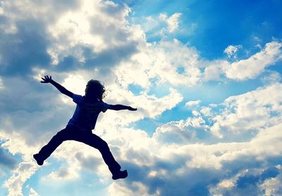 Low angle view of man jumping against cloudy sky