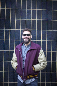 Portrait of smiling man with hands in pocket standing against pattern wall