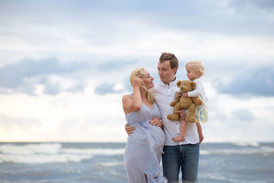 Couple with child holding stuffed toy at beach against sky