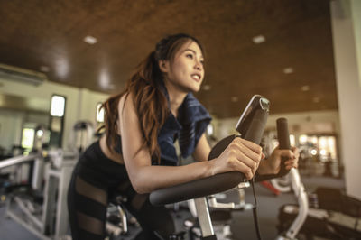 Low angle view of young woman exercising on bike in gym