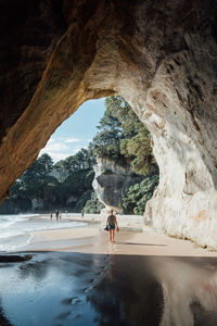 Rear view of woman walking on shore seen through cave