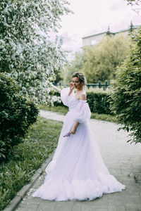 A beautiful delicate woman bride in a wedding dress walks alone in a blooming spring outdoor park