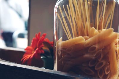 Close-up of uncooked pastas in glass by flower container 