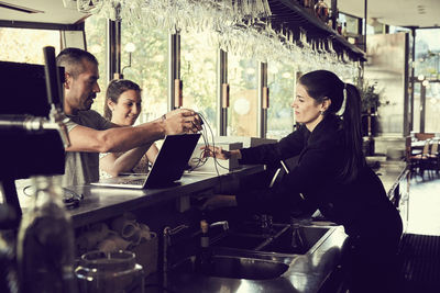 Woman and man giving cable to female owner in cafe