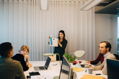 Confident businesswoman showing box to multi-ethnic colleagues sitting in board room at creative office