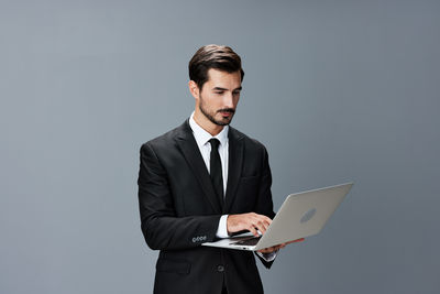 Young man using laptop while standing against blue background