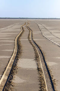 Tire tracks on sand dune against sky