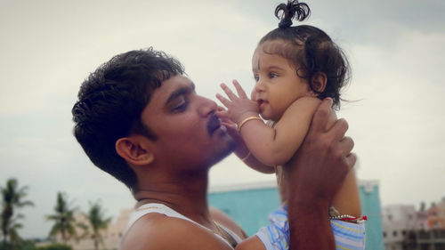 Side view of father carrying cute shirtless daughter while standing against sky