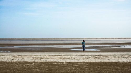 Full length of young woman walking at beach against sky during sunny day