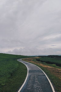 Empty road amidst field against sky