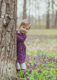 Portrait of young woman standing by tree trunk