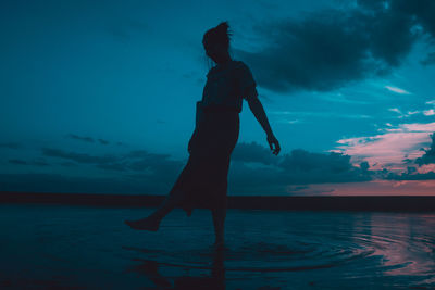 Silhouette man standing in sea against sky during sunset