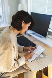 Businesswoman writing in note pad on table at home