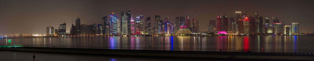 Illuminated modern buildings by river at night