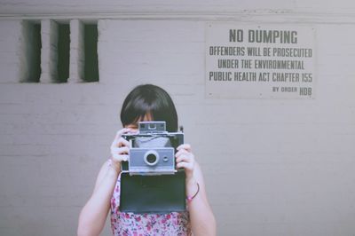 Woman photographing from camera while standing against wall with text