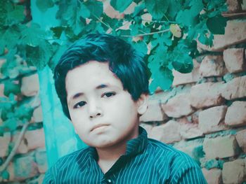 Portrait of boy with green leaves against wall
