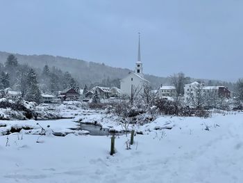 Snow covered houses by buildings against sky