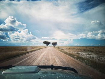 Road amidst field seen through car windshield