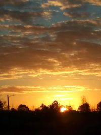 Silhouette trees against dramatic sky during sunset