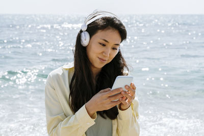 Young woman using phone while standing on sea