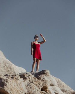 Full length portrait of woman standing on rock against clear sky