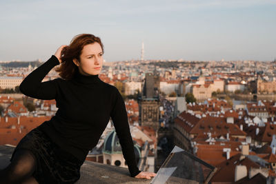 Young woman looking at city buildings against sky