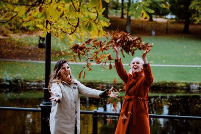 Happy friends playing with dry leaves at park