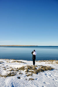 Rear view of man standing on shore against clear sky
