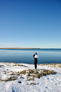 Rear view of man standing on shore against clear sky