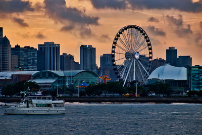 Ferris wheel by river against buildings in city