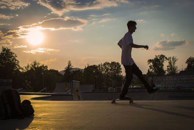 Full length of man skateboarding in park against sky during sunset