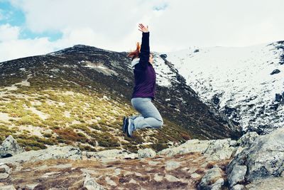 Side view of woman jumping with arms raised on mountain during winter