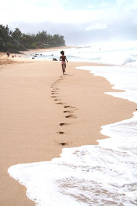 Rear view of girl running at beach against sky