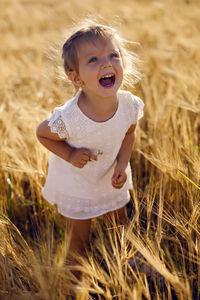 Little girl is happy on the field with ears in the evening sunset in summer.